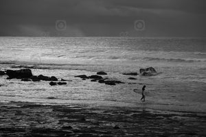 Black and white photograph of a surfer entering the water at Mollymook NSW